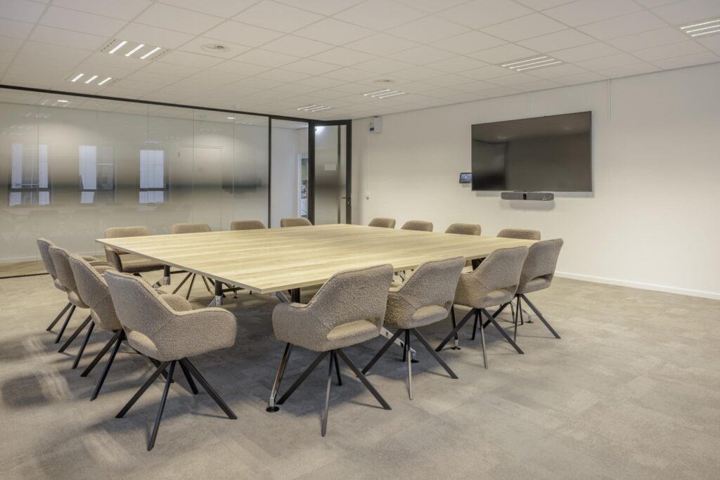 Modern conference room on Hiridostraat with a large wooden table, beige chairs, and a wall-mounted screen.